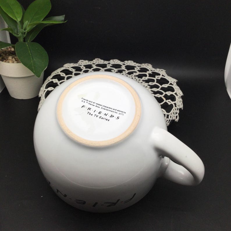 Puede incluir: Taza de cer&aacute;mica blanca con un logotipo de Friends negro y el texto "Friends The TV Series" en la parte inferior.