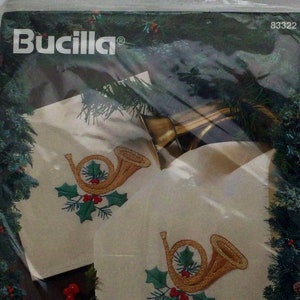 Puede incluir: Un juego de ocho servilletas de punto de cruz estampadas con un cuerno franc&eacute;s dorado con acebo y bayas rojas. Las servilletas est&aacute;n empaquetadas en una bolsa de pl&aacute;stico transparente con un anillo dorado en la parte superior. El paquete tambi&eacute;n incluye el texto "Bucilla&reg;" y "Angels of Christmas".