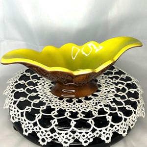 May include: A yellow and brown ceramic bowl with a leaf-shaped design. The bowl is on a white lace doily.
