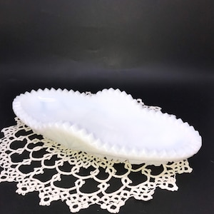 May include: White milk glass serving dish with a scalloped edge. The dish is oval shaped and has a slightly curved bottom.