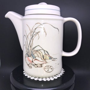 May include: White ceramic teapot with a seashell and seaweed design. The teapot has a lid and a handle.