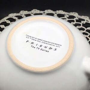 Puede incluir: Taza de cer&aacute;mica blanca con el logotipo de Friends y el texto "Friends and all related characters and elements &copy; & &trade; Warner Bros. Entertainment Inc. (s17) FRIENDS The TV Series" en la parte inferior.