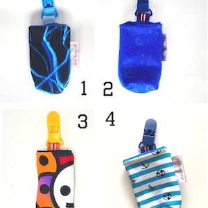 May include: Four pacifier clips with different fabric designs. The clips have a plastic clip at the top and a fabric pouch at the bottom. Designs include blue lightning, blue nautical, a skull, and blue and white stripes with anchors.
