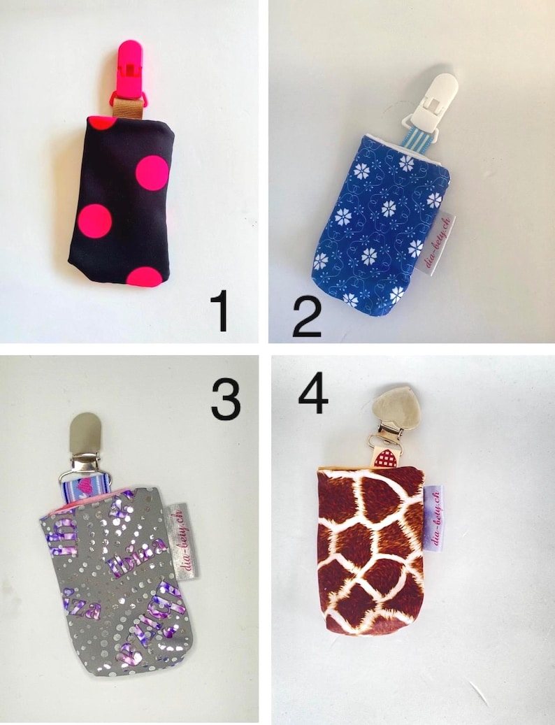 May include: Four baby pacifier holders with different patterns. One is black with pink polka dots, another is blue with white flowers, a third is gray with purple accents, and the last is brown with a giraffe print. Each has a clip.