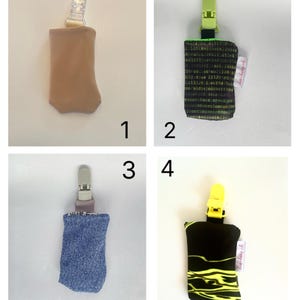 May include: A collage of four pacifier clips. The clips have different fabric designs: tan, black with green text, blue denim, and black with yellow squiggles. Each clip has a plastic clip at the top.