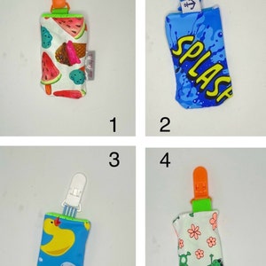 May include: Four pacifier clips with different fabric designs. One clip has a watermelon and ice cream pattern, another has a blue splash design with the word "SPLASH", a third has a yellow duck pattern, and the last has a frog and flower pattern.