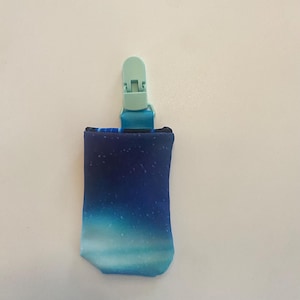 May include: A baby pacifier clip with a blue and white gradient fabric pouch, featuring a starry night design. The clip is a light green color.