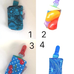 May include: Four pacifier clips with fabric pouches. The pouches feature various patterns: a blue and black swirl, a colorful fruit design, a blue cherry print, and a blue glitter pattern. Each clip has a different colored plastic clip.