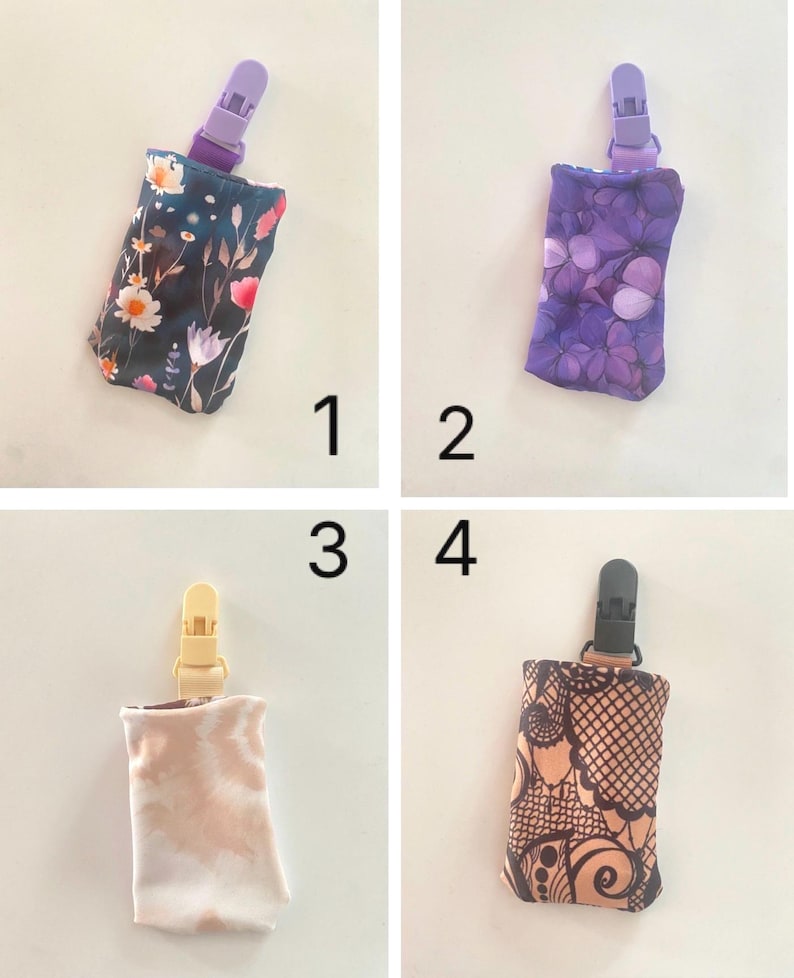 May include: Four fabric pacifier clips with different patterns. The clips have a plastic clasp at the top and a fabric pouch at the bottom. The patterns include floral, purple butterfly, tie-dye, and henna-style designs. The clips are numbered 1 through 4.