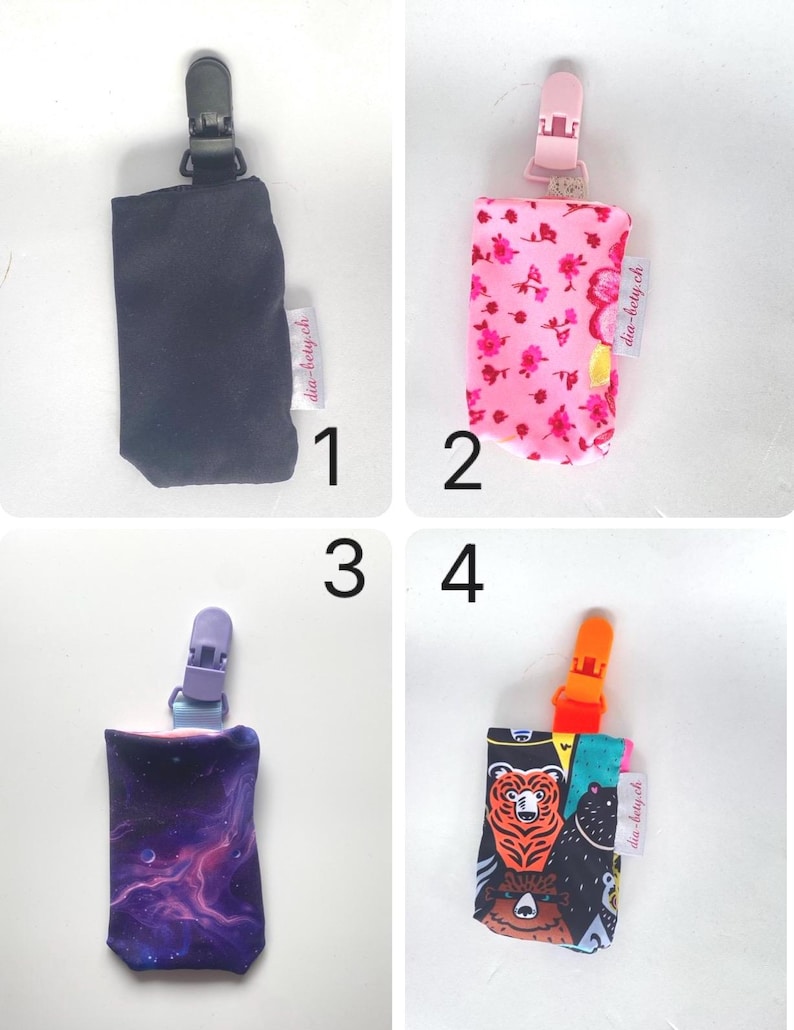 May include: Four different pacifier clips are displayed. The first is black, the second is pink with a floral pattern, the third is purple with a galaxy design, and the fourth is black with bear graphics. Each clip has a matching plastic clip.