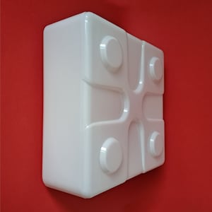 May include: White plastic square block with four round protrusions on the top and bottom. The block has a smooth, glossy finish.