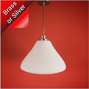 May include: A white glass pendant light with a wide, rounded, bell-shaped shade hanging from a silver cord against a red background. The light is available in brass or silver.