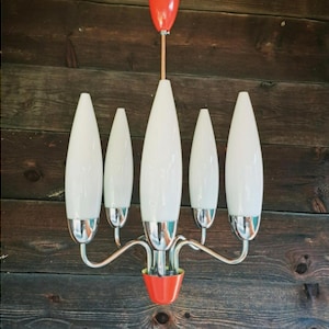May include: A mid-century modern chandelier with five white, teardrop-shaped glass shades. The fixture has a chrome finish with red accents on the top and bottom. The light hangs from a wooden ceiling.