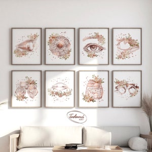 May include: Eight framed art prints featuring watercolor illustrations of eye anatomy and optometry tools, adorned with floral arrangements in neutral tones. The prints are displayed on a white wall above a sofa.