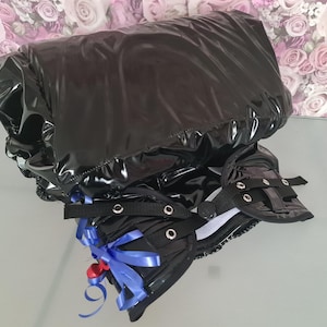 Puede incluir: Prenda de cuero patentado negro con una cinta azul y un arnés blanco y negro con hebillas plateadas.