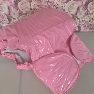 Puede incluir: Una cubierta de pañal de vinilo rosa con un diseño acolchado. La cubierta tiene una cintura elástica blanca y un forro blanco.