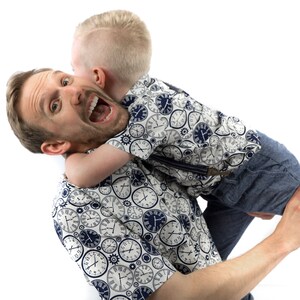 May include: A man and a young boy are laughing and hugging. The man is wearing a white shirt with a blue and white clock pattern. The boy is wearing a blue and white shirt with a clock pattern and blue jeans.