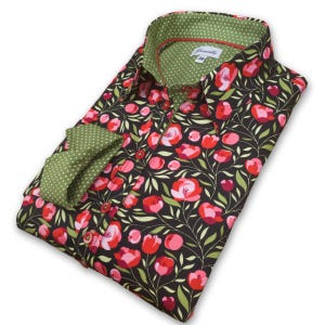 May include: A folded shirt with a floral design. The shirt has a black base with red and pink flowers and green leaves. The collar and cuffs are green with white polka dots. The shirt has red buttons.