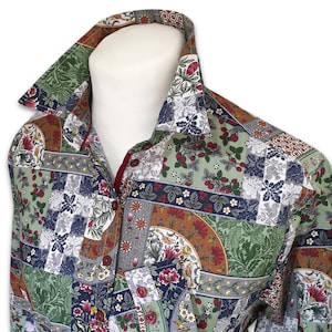Könnte beinhalten: Ein langärmeliges Hemd mit Knopfleiste und einem mehrfarbigen Patchwork-Muster. Das Design zeigt verschiedene botanische Motive, Erdbeerpflanzen und florale Elemente in Grün-, Rot-, Weiß- und Brauntönen mit dunkelroten Knöpfen.