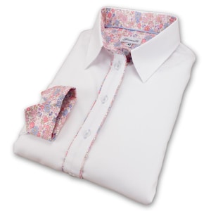 Puede incluir: Camisa blanca de manga larga con cuello y puños de estampado floral. La camisa tiene cierre de botones en la parte delantera y una pequeña etiqueta que dice "Damarisco" con la talla "40" impresa en ella.