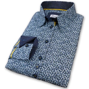 May include: A blue long-sleeved shirt with a white floral pattern. The shirt has a yellow trim on the collar and cuffs, and a navy blue and white polka dot lining on the inside of the collar and cuffs.