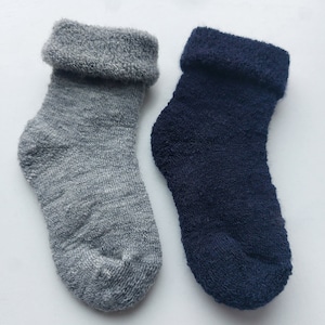 Może przedstawiać: Dwie pary skarpet, jedna szara, a druga granatowa. Skarpety są wykonane z miękkiego, puszystego materiału i mają podwinięty ściągacz.