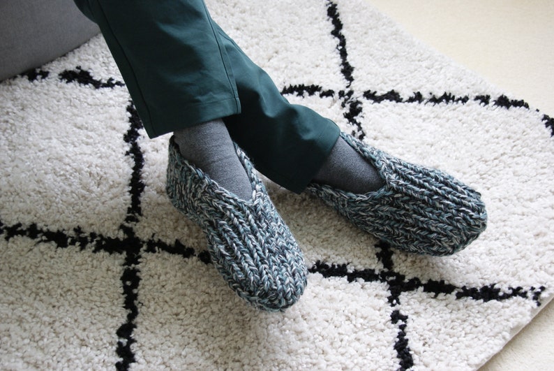Puede incluir: Un par de zapatillas de punto azul y blanco con una abertura en forma de V en la parte superior. Las zapatillas se llevan puestas en los pies.