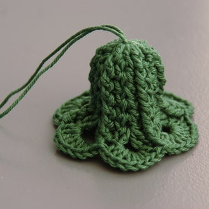 Puede incluir: Un adorno de campana de ganchillo verde con una cuerda larga.