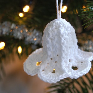 Puede incluir: Adorno de campana de crochet blanco colgado de un &aacute;rbol de Navidad. La campana tiene un dise&ntilde;o delicado y de encaje y es una decoraci&oacute;n navide&ntilde;a tradicional.