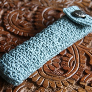May include: A light blue crocheted pencil case with a flap closure and a silver button.