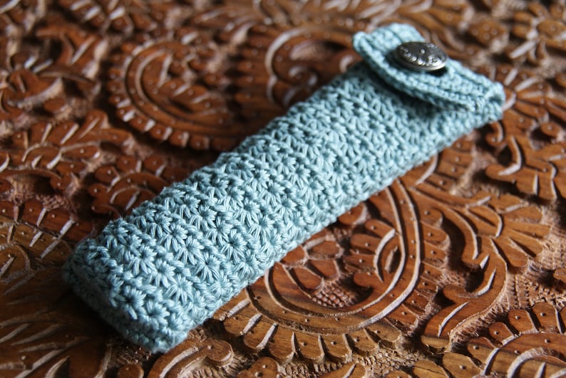 May include: A light blue crocheted pencil case with a flap closure and a silver button.