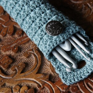 May include: A blue crocheted case with a silver button, holding a set of crochet hooks.