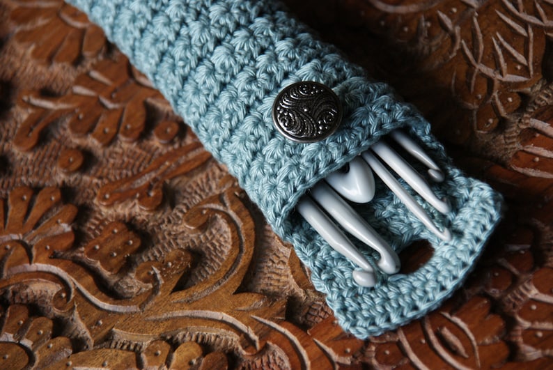 May include: A blue crocheted case with a silver button, holding a set of crochet hooks.