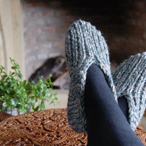 Puede incluir: Un par de zapatillas de punto acogedoras en un esquema de color azul y blanco. Las zapatillas son usadas por una persona que se relaja cerca de una chimenea.