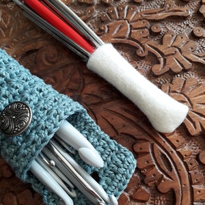 May include: A blue crocheted case with a silver button holds a set of crochet hooks. A white felt case holds a set of knitting needles.