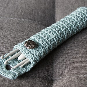 May include: A light blue crocheted case with a silver button closure, holding a set of white crochet hooks.