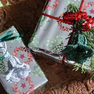 Puede incluir: Dos cajas de regalo plateadas envueltas con cinta verde y roja y decoradas con guirnaldas y estrellas verdes y rojas. Cada caja tiene un adorno de campana de ganchillo.