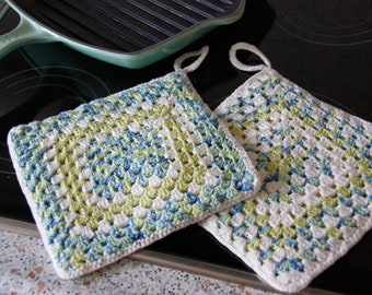 Puede incluir: Dos agarraderas de olla de ganchillo en un esquema de colores blanco, verde y azul. Las agarraderas de olla están hechas con un patrón de cuadrado de la abuela.