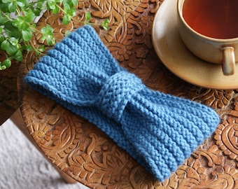 May include: A blue knitted headband with a bow knot. The headband is on a wooden surface with intricate carvings.