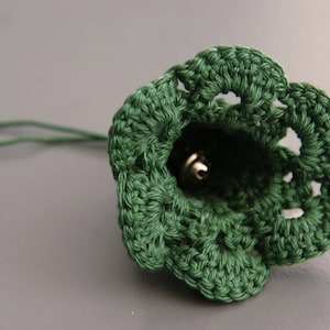 Puede incluir: Una campana de crochet verde con una campana de plata en su interior. La campana est&aacute; unida a una cuerda verde.