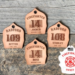May include: Five leather firefighter helmet keychains with different names and numbers. The keychains are brown and have a distressed look. The keychains are on a wooden background.