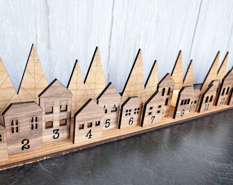 May include: Wooden Advent calendar shaped like a town with houses and trees. The houses have numbers from 1 to 15.