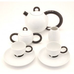 May include: A white porcelain tea set with black handles. The set includes a teapot, creamer, sugar bowl, and two teacups and saucers.