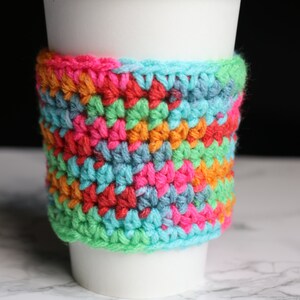 May include: A colorful crocheted coffee cup cozy with a geometric pattern in shades of pink, orange, green, blue, and turquoise.