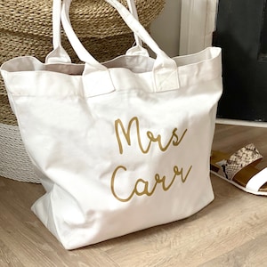 May include: White canvas tote bag with gold lettering that says "Mrs. Carr"