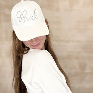 May include: A white baseball cap with the word "Bride" embroidered in silver on the front.