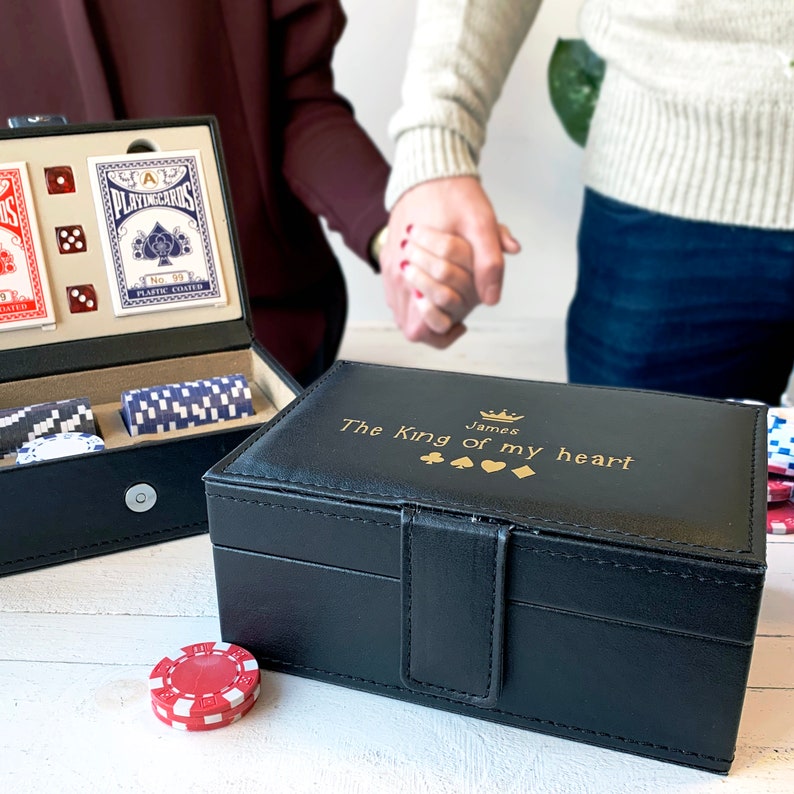May include: A black leather box with a gold inscription that reads "James The King of my heart" with a crown and four playing card suit symbols. The box is closed and sitting on a wooden surface.