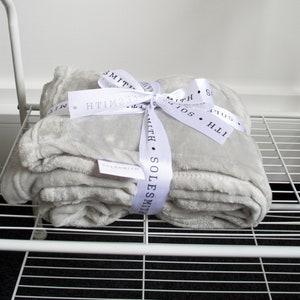 May include: A gray plush throw blanket tied with a white satin ribbon. The ribbon has the text "SOLESMITH" printed on it.