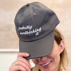 May include: A grey baseball cap with the text "probably overthinking it" embroidered in white on the front.