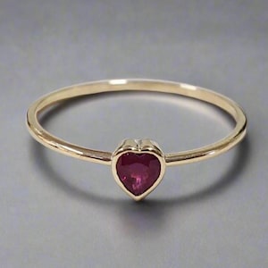 May include: A gold band ring with a heart-shaped ruby gemstone.